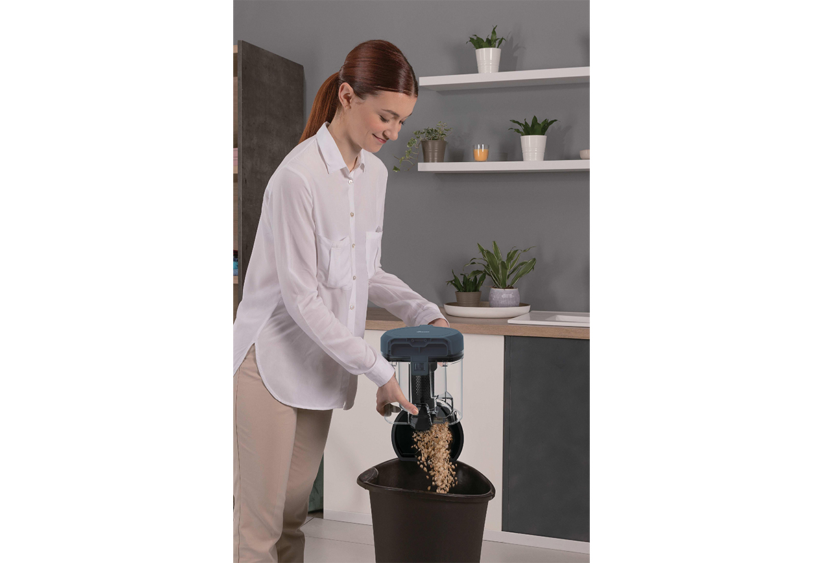 Μια γυναίκα αδειάζει τον κάδο της σκούπας σε έναν κάδο απορριμάτων.